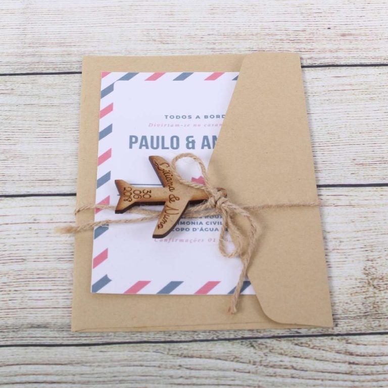 Convite de casamento com envelope de papel kraft, decorado com uma fita de sisal e um pequeno avião de madeira, colocado sobre uma superfície de madeira clara.