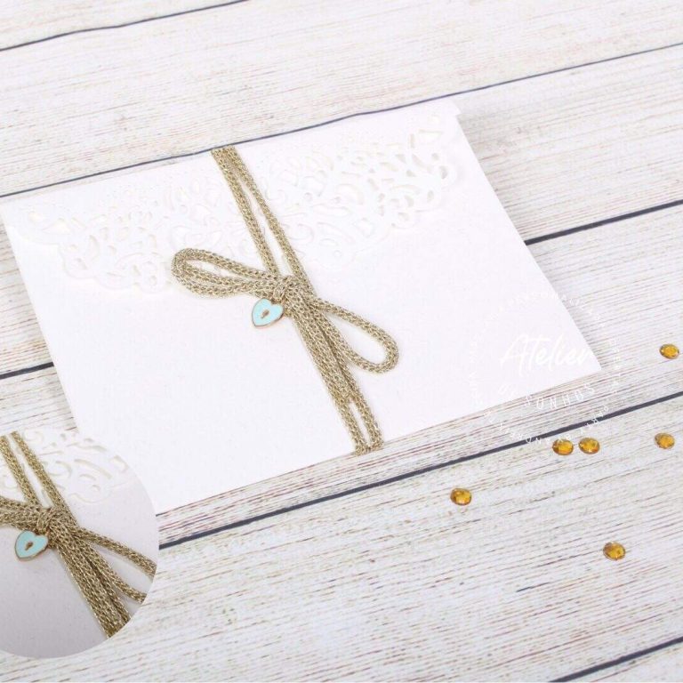 Caixa de presente branca com laço dourado e detalhe de coração azul, sobre uma superfície de madeira clara, com pequenos confetes dourados ao redor.