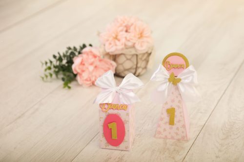Decoração de aniversário de 1 ano com flores cor-de-rosa, laços brancos e detalhes dourados, ideal para festas infantis.
