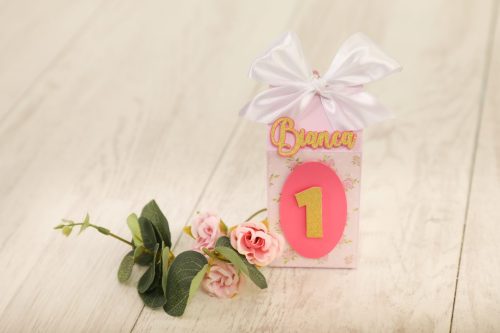 Cadeirão de papel decorativo com o nome "Bianca" e o número "1" em destaque, decorado com fita de cetim branca e flores de papel rosa, ideal para celebrações infantis.