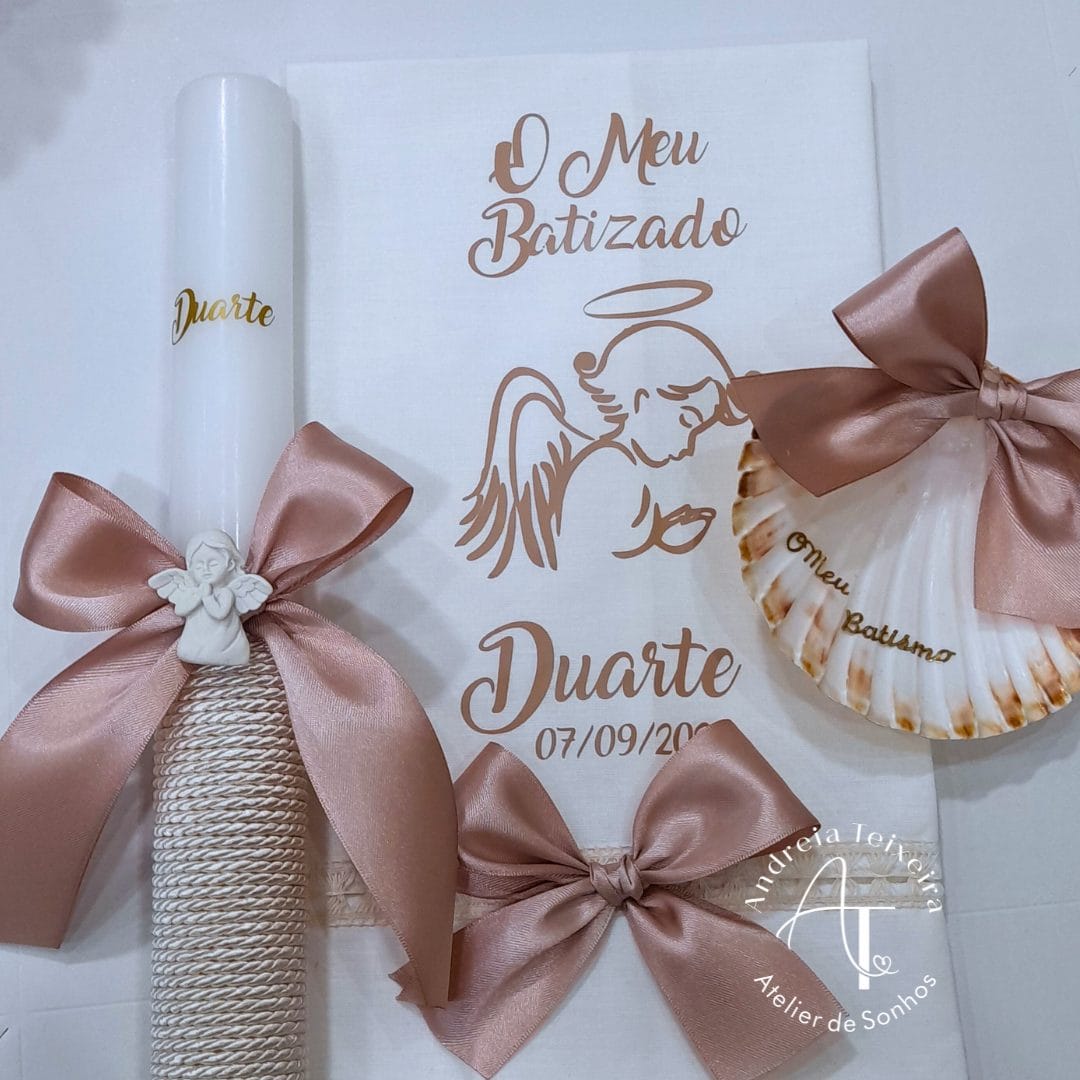 Luminária de vela decorativa com laços de fita rosa, ideal para celebrações de batizado, com uma concha decorativa e uma folha de papel com desenho de anjo e texto em português.