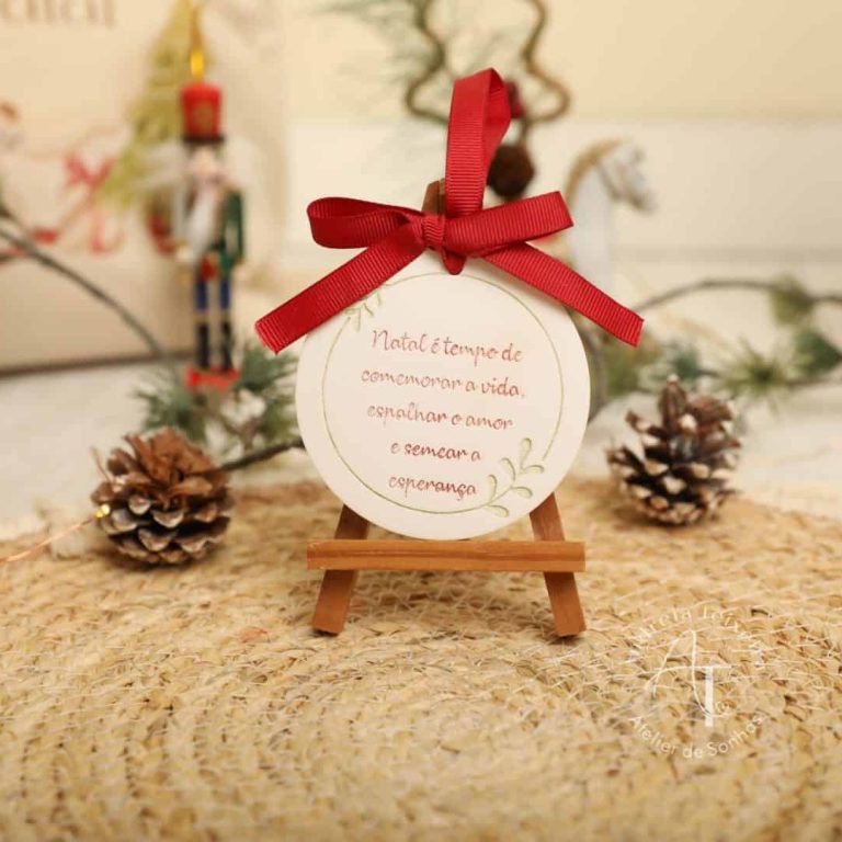 Pequeno quadro decorativo com mensagem de esperança, decorado com fita vermelha, rodeado de pinhas e elementos natalícios, ideal para decoração de Natal ou presentes festivos.