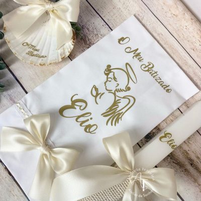 Vela, toalha e concha de batizado personalizadas com anjo em foil dourado e laços em cetim creme.