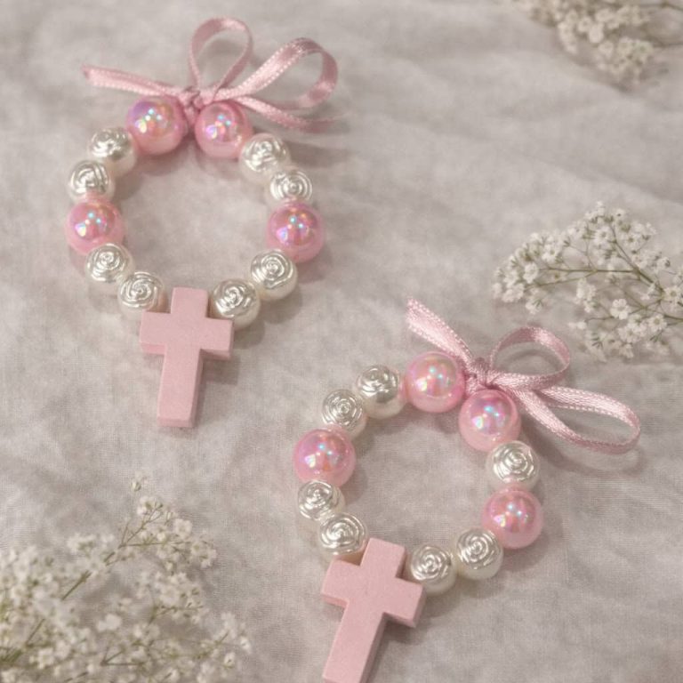 Pulseira de bebê com contas de pérola rosa e branca, decorada com laços de fita rosa e pingentes de cruz, ideal para ocasiões especiais ou como lembrança religiosa.