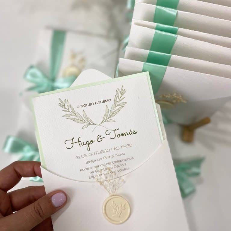 Convite de batizado botânico oliveira com envelope texturado branco, fita verde sálvia, lacre branco e ramo preservado.