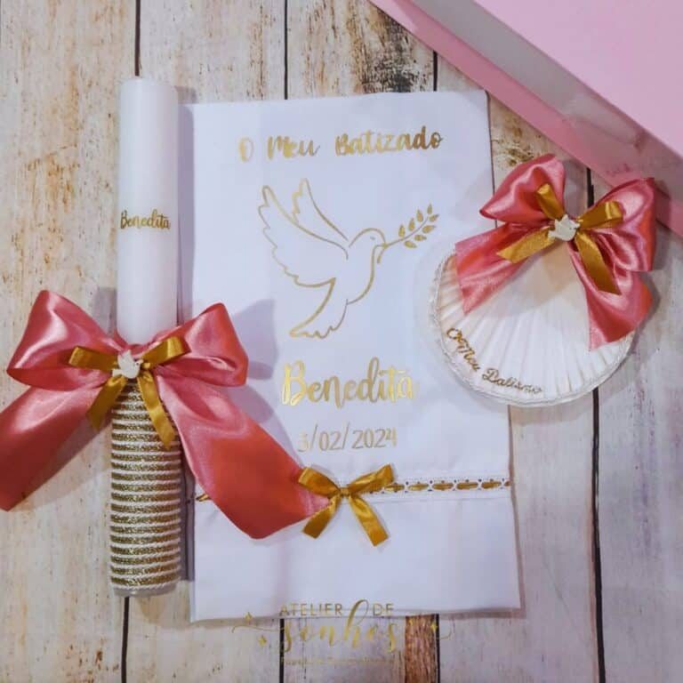 Design sem nome (16) Vara de batismo com detalhes dourados, uma vela decorativa com laço rosa e dourado, e um livro de orações com uma ilustração de pomba e a data do batismo, tudo disposto sobre uma superfície de madeira.