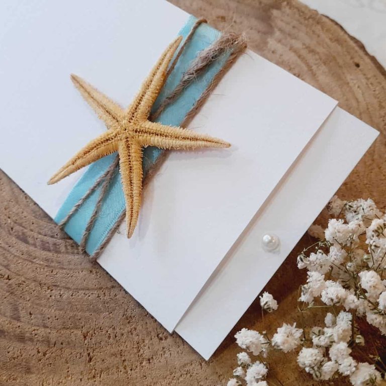 Estrela-do-mar, carta azul e flores secas sobre uma tábua de madeira, criando uma composição de tema marítimo e natural.