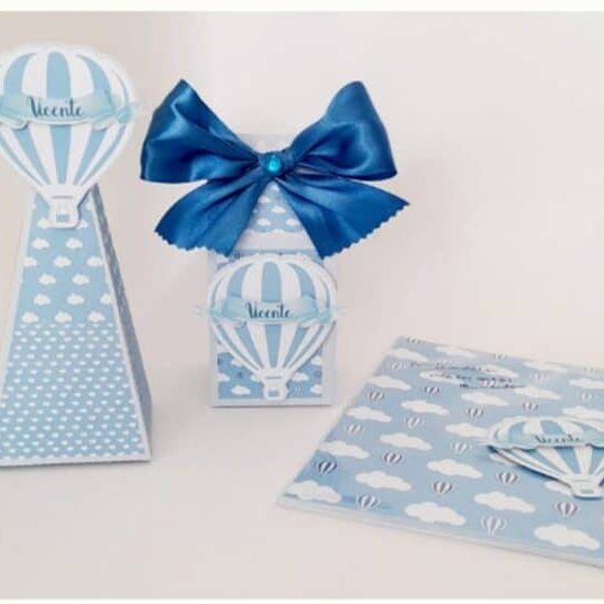 Brinquedos decorativos de papel com tema de balão de ar quente, incluindo uma caixa com laço azul, uma torre de papel e uma caixa de presente, todos com detalhes em azul e branco.
