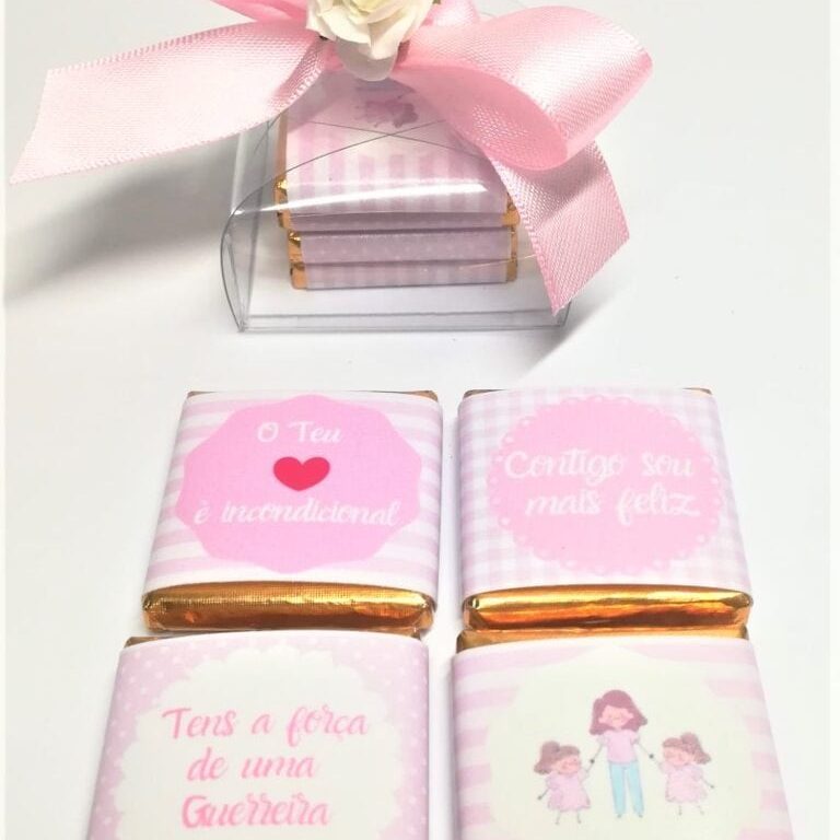 Caixa de chocolates decorada com fita rosa, laço e flor branca, acompanhada de quatro chocolates embrulhados com mensagens de incentivo e amor, ideal para presente.