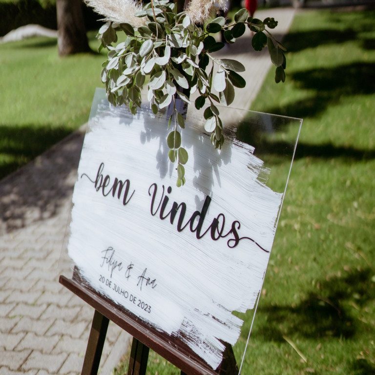 atelier de sonhos artigos de casamento estacionario (2) Placa acrílica de boas-vindas da Coleção Sopro para casamento com fundo pincelado a branco assente num cavalete de madeira escura.