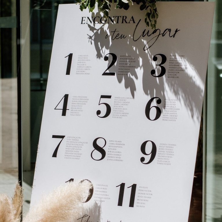 atelier de sonhos artigos de casamento estacionario (3) Quadro de assentos para casamento com lista numerada e decoração com plantas e flores secas, em ambiente ao ar livre.