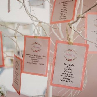 Balde de árvores decorativas com cartões pendurados, cada um com nomes e mensagens, em tons de rosa e branco, ideal para eventos como casamentos ou celebrações familiares.