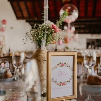 Lata de vidro com flores brancas e rosas, decorando uma mesa de evento com ambiente rústico e elegante, com detalhes de vidro e velas ao fundo.