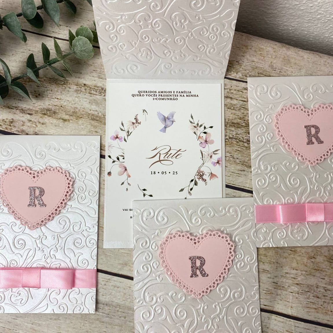 Cadeado de coração rosa com letra "R" em relevo, decorado com fita de cetim rosa, em convite de casamento com fundo branco com relevo delicado.